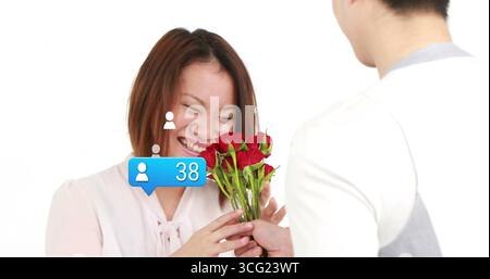 Homme chinois présentant un bouquet de roses rouges à une femme souriante en studio, avec notification numérique Banque D'Images