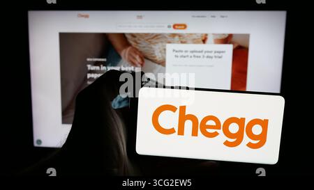 Dans cette illustration photo, une personne tient un téléphone portable avec le logo de la société américaine de technologie éditoriale Chegg Inc sur l'écran devant la page Web. Banque D'Images