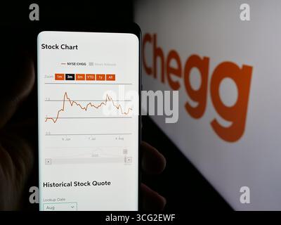 Dans cette illustration photo, une personne tient un smartphone avec la page web de la société américaine de technologie éditoriale Chegg Inc sur l'écran devant le logo. Banque D'Images
