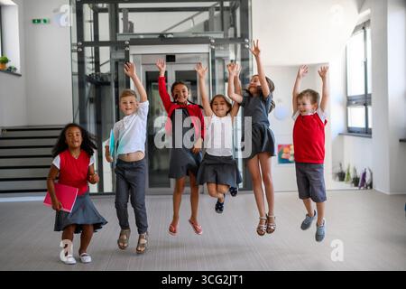 Groupe d'écoliers en uniforme, sautant dans le couloir de l'école. Banque D'Images
