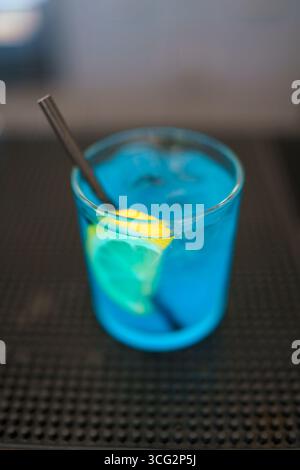 Un cocktail bleu rafraîchissant servi dans un verre avec un coin citron et une paille sur un comptoir sombre parfait pour une fête d'été ou une occasion spéciale Banque D'Images