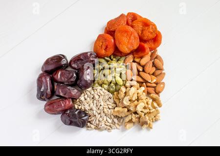 Dattes, abricots séchés, graines de citrouille, graines de tournesol, amandes, noix sur un fond en bois blanc. Nourriture saine, collations. Concept de régime végétarien. Banque D'Images