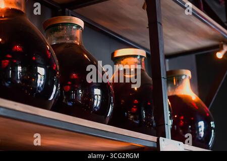 Les bocaux avec un couvercle de vin rouge sont stockés dans la cave, le vin fait maison est sur une étagère en bois Banque D'Images