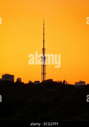 Tour de télévision au coucher du soleil. Horizon urbain avec antenne tour radio contre ciel orange. Banque D'Images