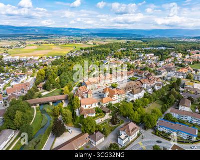 Vue aérienne du pont en bois historique qui s'étend sur la rivière sinueuse, niché au milieu des bâtiments aux toits rouges et de la végétation luxuriante de la ville pittoresque, Aarberg, Canton de Berne, Suisse. Banque D'Images
