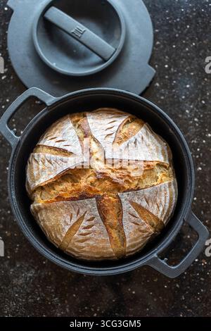 Pain au levain fraîchement cuit dans un four hollandais en fonte noire. La croûte dorée rustique présente un motif de notation artistique, mettant en valeur le fait à la main Banque D'Images