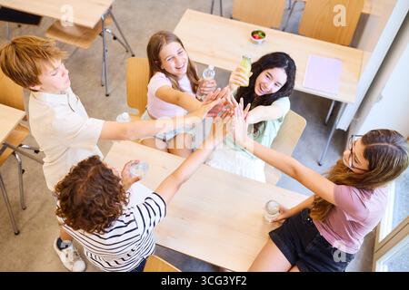 Les élèves énergiques partagent le rire et la positivité en portant un toast avec des boissons dans un environnement scolaire lumineux. La scène animée représente youthfu Banque D'Images