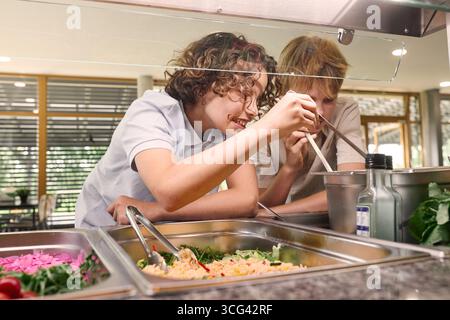 Les élèves apprécient la sélection d'aliments sains dans une cafétéria d'école, mettant en valeur le travail d'équipe et le choix Banque D'Images