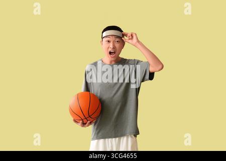 Surpris jeune homme asiatique avec des lunettes AR et balle pour jouer au basket-ball sur fond vert Banque D'Images