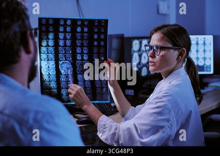 Jeune femme adulte caucasienne expliquant les résultats du scan cérébral à un homme d'âge moyen Banque D'Images