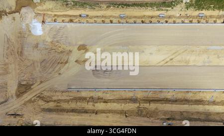 Vue aérienne de haut en bas d'un chantier de construction d'autoroute, montrant les travaux de terrassement, le nivellement du sol et la préparation des fondations pour de nouvelles infrastructures routières et t Banque D'Images