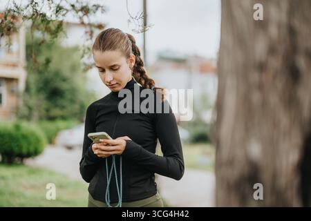Jeune femme envoyant des SMS sur son téléphone alors qu'elle portait une tenue de fitness à l'extérieur Banque D'Images