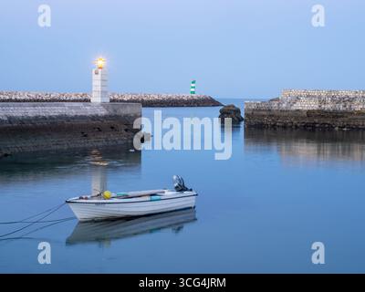 Petit bateau de pêche amarré dans l'eau calme près de l'entrée du port au coucher du soleil, phare en arrière-plan. Lagos, Algarve, Portugal, 13 mai 2017. Banque D'Images
