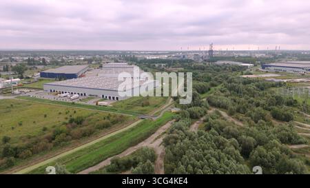 Vue aérienne grand angle d'un parc industriel moderne et centre d'entrepôt de distribution entouré de ceintures vertes, représentant la logistique urbaine, trad global Banque D'Images