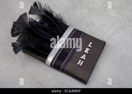 cadeau enveloppé dans du papier noir avec des rubans et des plumes le décorant avec nom personnalisé en lettres en bois Banque D'Images