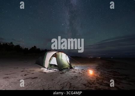 Une tente de camping illuminée sur une plage de sable estonienne sous le spectaculaire ciel étoilé et la galaxie de la voie Lactée. Banque D'Images