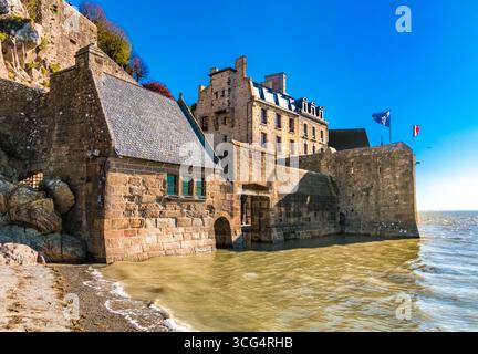 Un gros plan saisissant de la première porte d’entrée du Mont‑Saint‑Michel, la porte de l’avance construite en granit, et ses murs fortifiés, debout au milieu des eaux de crue... Banque D'Images