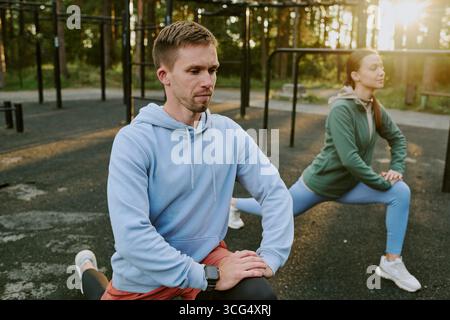 Jeune homme caucasien et femme s'étirant à l'extérieur pendant l'entraînement matinal Banque D'Images