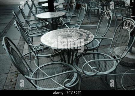 Café en plein air avec tables rondes en mosaïque et chaises en métal, disposées en rangées sur le trottoir de la ville. Ambiance gastronomique européenne. Banque D'Images