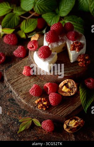 Camembert avec framboises fraîches et noix sur une table vintage brune. Banque D'Images