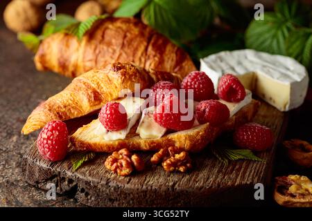 Croissant au camembert, framboises fraîches et noix sur une table vintage brune. Banque D'Images
