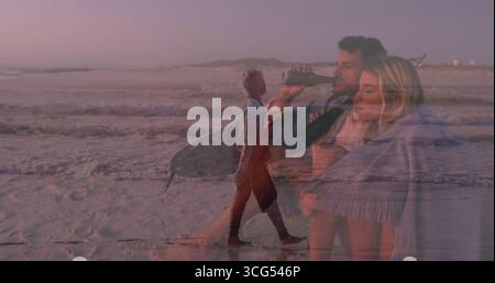 Couple serrant sirotant une bouteille sombre au rivage au crépuscule, avec couverture frangée et ciel pastel Banque D'Images