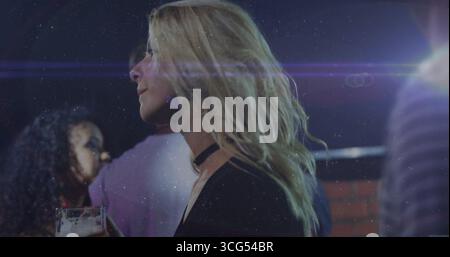 Femme blonde portant un haut noir et un choker tenant un verre de bière au bar, avec un éclat de lentille Banque D'Images