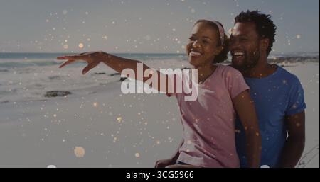 Pointage femme dans le bandeau de t-shirt rose, homme dans le t-shirt bleu embrassant sur la plage de sable avec des étincelles Banque D'Images