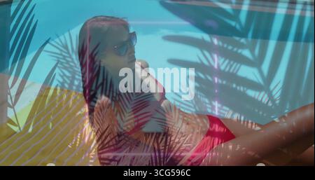 Femme chinoise couchée portant des nuances de bikini rouges sur une chaise longue près de la piscine turquoise, montrant des ombres de palmier Banque D'Images