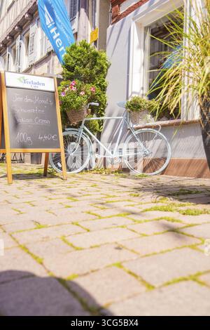 Vélo avec paniers de fleurs et tableau noir devant un café au soleil, petite ville de Perle Calw, district de Calw, Allemagne Banque D'Images