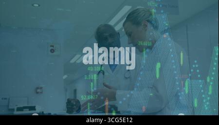 Médecins examinant les cartes numériques dans le couloir près du poste de soins infirmiers, avec tablette et stylo Banque D'Images