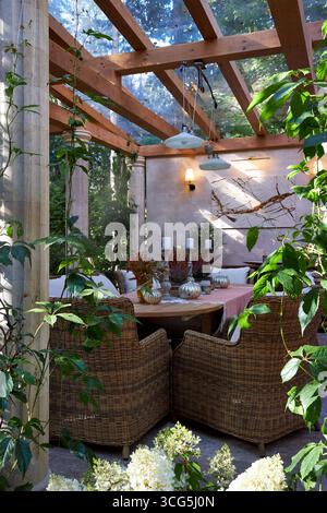 Coin salon extérieur élégant avec fauteuils en osier, coussins blancs et oreillers orange. Table en bois décorée de bougies, de plantes et de détails d'automne Banque D'Images