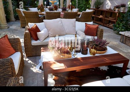 Coin salon extérieur élégant avec fauteuils en osier, coussins blancs et oreillers orange. Table en bois décorée de bougies, de plantes et de détails d'automne Banque D'Images