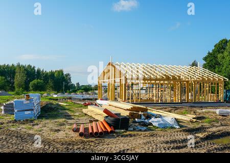 Nouvelle maison moderne en bois en construction avec ossature en bois visible, poutres de toit et matériaux de construction dispersés autour du site Banque D'Images