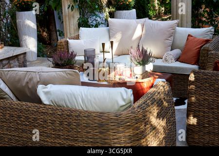 Coin salon extérieur élégant avec fauteuils en osier, coussins blancs et oreillers orange. Table en bois décorée de bougies, de plantes et de détails d'automne Banque D'Images
