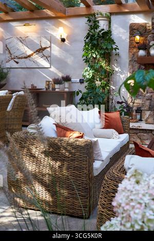 Coin salon extérieur élégant avec fauteuils en osier, coussins blancs et oreillers orange. Table en bois décorée de bougies, de plantes et de détails d'automne Banque D'Images