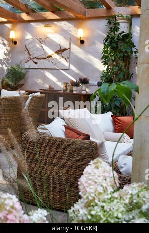 Coin salon extérieur élégant avec fauteuils en osier, coussins blancs et oreillers orange. Table en bois décorée de bougies, de plantes et de détails d'automne Banque D'Images