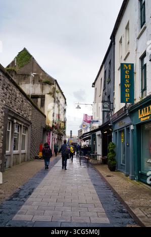 Une journée couverte dans une rue étroite en Irlande, les gens marchant devant des magasins avec des auvents. Banque D'Images