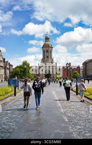 Les gens se promènent le long d'un sentier pavé vers un bâtiment historique à Dublin, en Irlande, sous un ciel bleu vif. Banque D'Images