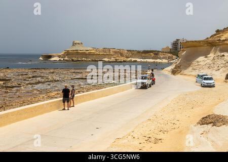 Gozo, Malte – 23 juin 2021 : les touristes se tiennent près des marais salants tandis qu’une voiture roule le long de la route côtière. Banque D'Images