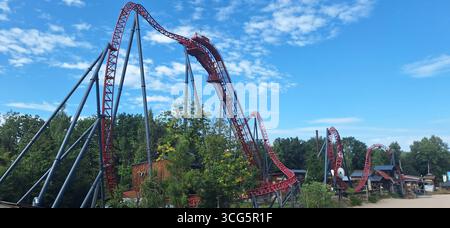 En milieu d'après-midi, les visiteurs profitent d'une balade palpitante sur une montagne russe torsadée entourée de verdure dans un parc d'attractions sous un ciel bleu vif Banque D'Images