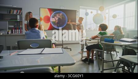 Garçon d'école élémentaire avec ordinateur tablette donnant présentation sur le système solaire et les planètes devant les camarades de classe et l'enseignant à l'aide de l'écran numérique. Smart Kids étudier l'astronomie spatiale en classe. Banque D'Images
