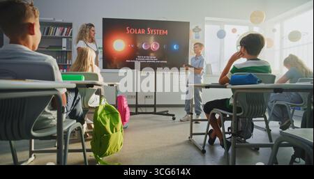 Garçon d'école élémentaire avec ordinateur tablette donnant présentation sur le système solaire et les planètes devant les camarades de classe et l'enseignant à l'aide de l'écran numérique. Smart Kids étudier l'astronomie spatiale en classe. Banque D'Images
