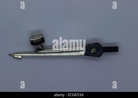 Gros plan d'un compas crayon classique reposant sur une surface blanche et propre. Outil de dessin traditionnel utilisé pour dessiner des cercles et des arcs dans la géométrie. Banque D'Images