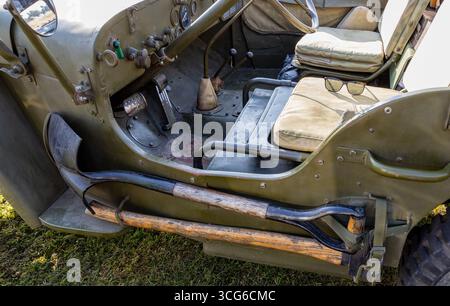 Vue intérieure d'une vieille jeep militaire montrant le siège du conducteur et le tableau de bord avec des outils rustiques attachés sur le côté Banque D'Images