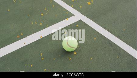 Balle de tennis jaune-vert reposant sur un terrain extérieur, avec des lignes blanches et des confettis étoiles dorées Banque D'Images