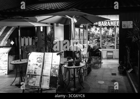 Photographie en noir et blanc d'une salle à manger extérieure en soirée avec des clients appréciant un repas, créant une atmosphère pittoresque et calme, Ponchaco, Nakag Banque D'Images