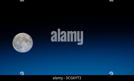 Une pleine lune est photographiée depuis la Station spatiale internationale. La Lune s'attarde à gauche de l'image, avec un horizon de lueur bleue de la Terre divisant l'image presque en deux, se fondant dans le noir de l'espace. 30 septembre 2023 une version optimisée d'une image originale de la NASA : crédit NASA Banque D'Images