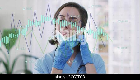 Travailleur de la santé dans les gommages bleus tirant vers le bas le masque chirurgical dans le couloir médical, avec des graphiques de données Banque D'Images