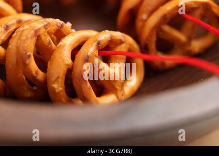 Craquelins de bretzels salés avec des cristaux de sel enfilés sur une corde rouge dans un bol en bois Banque D'Images
